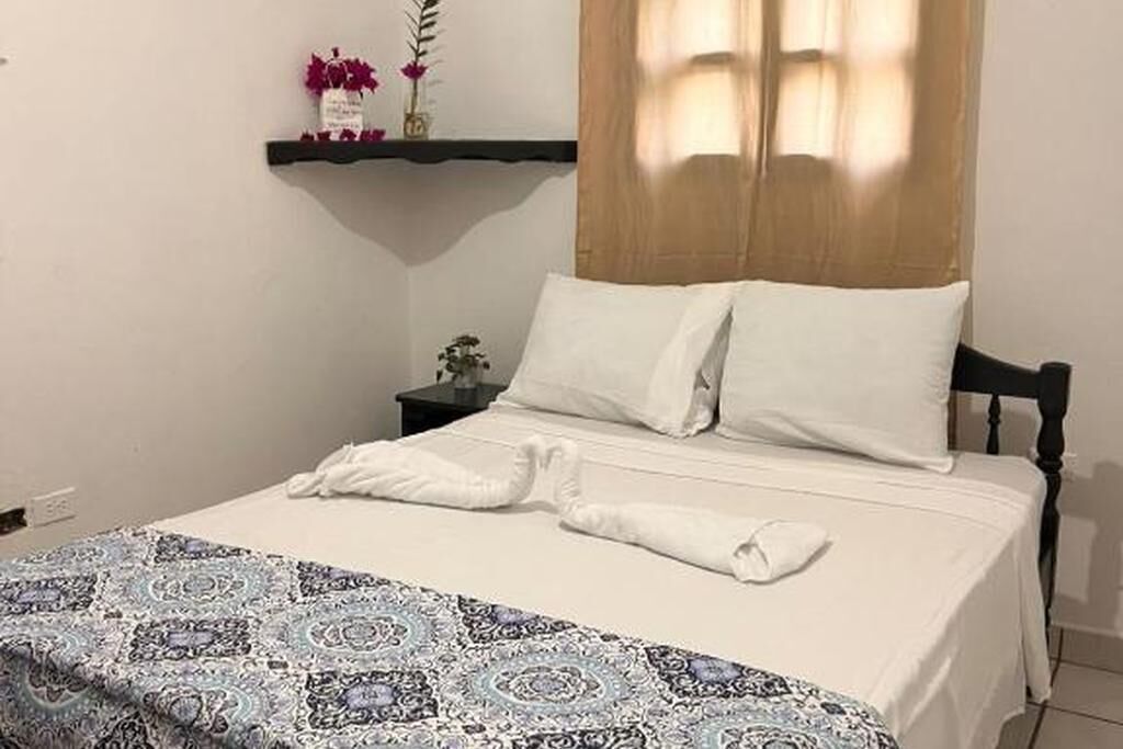 Una cama bien hecha con sábanas blancas, una manta decorativa estampada y un cabecero de madera.