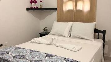 Una cama bien hecha con sábanas blancas, una manta decorativa estampada y un cabecero de madera.