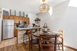 A modern kitchen with a stone island, wooden cabinets, a stainless steel refrigerator, and a dining area with a round table and chairs. - Secluded Townhome 15 min from Downtown (Galena)
