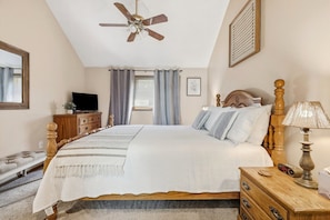 A bedroom with a bed, a wooden dresser, a nightstand, a ceiling fan, a window with curtains, a framed picture, and a television on a dresser. - Secluded Townhome 15 min from Downtown (Galena)