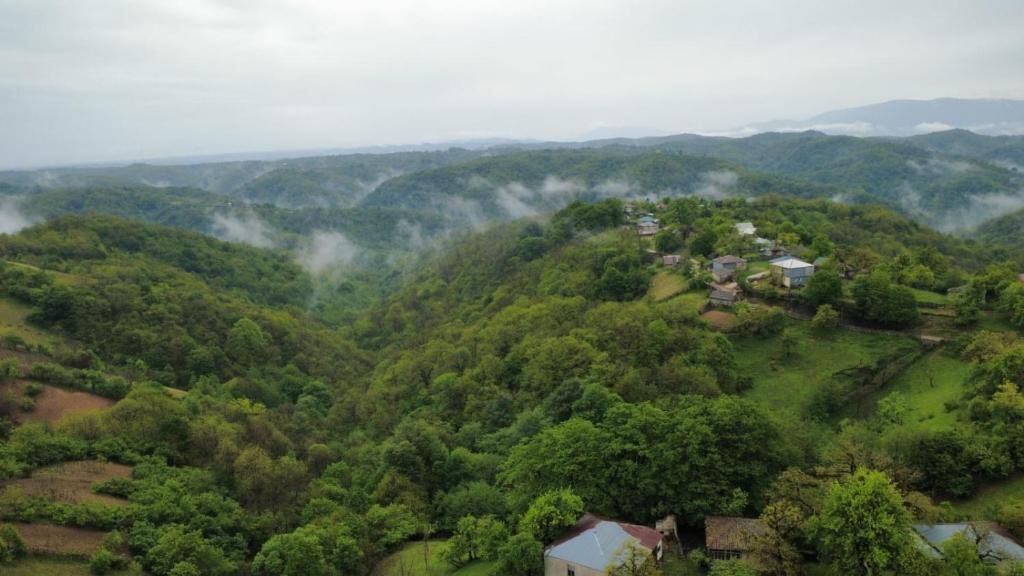 A hilly landscape with scattered houses and dense greenery.