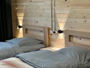 A wooden cabin-style room with two beds, each with striped bedding, and a small table. - Tea Gezruli (Gezruli)