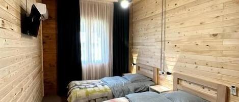 Een kamer met houten lambrisering, twee bedden, een plafondlamp en een raam met gordijnen.