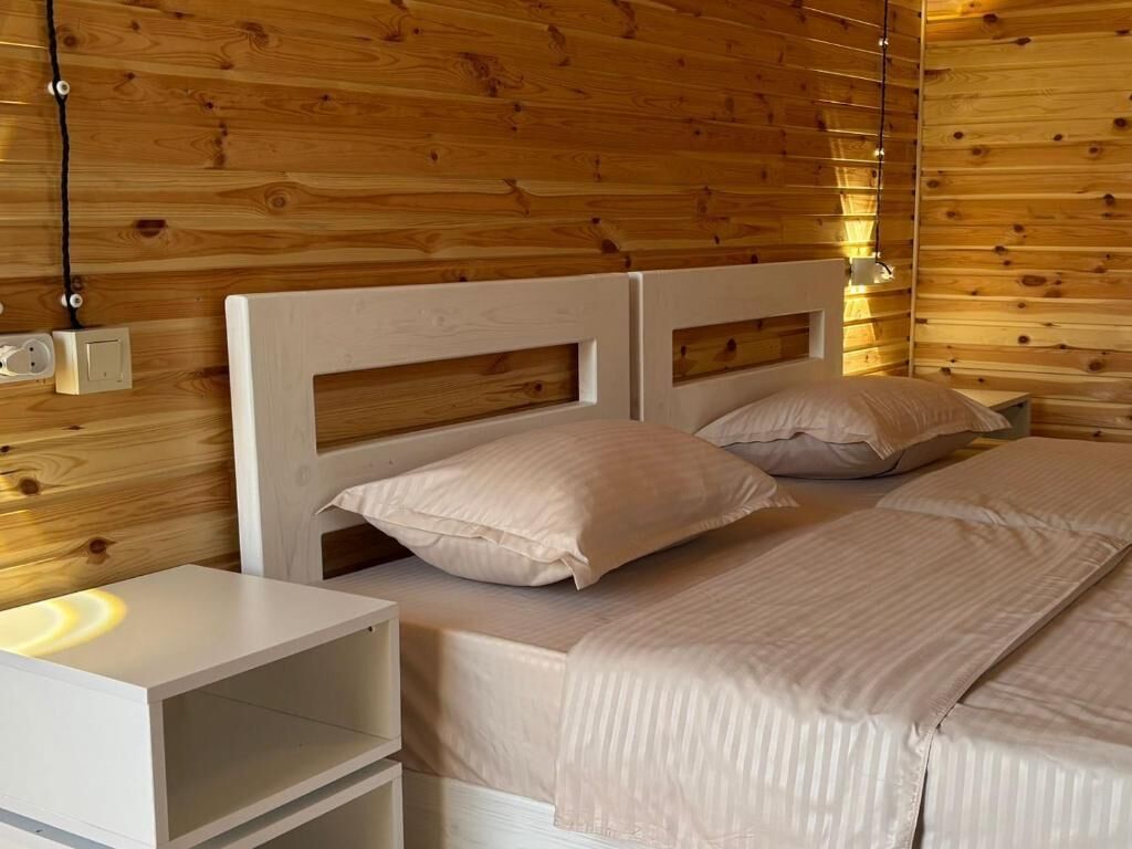 A wooden-paneled room with two beds, a bedside table, and a wall socket.