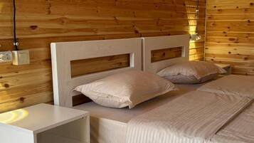 A wooden-paneled room with two beds, a bedside table, and a wall socket.