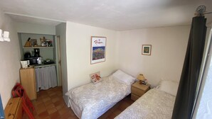 Ein kleines Zimmer mit zwei Betten, einer Küchenzeile und einem gerahmten Bild an der Wand.