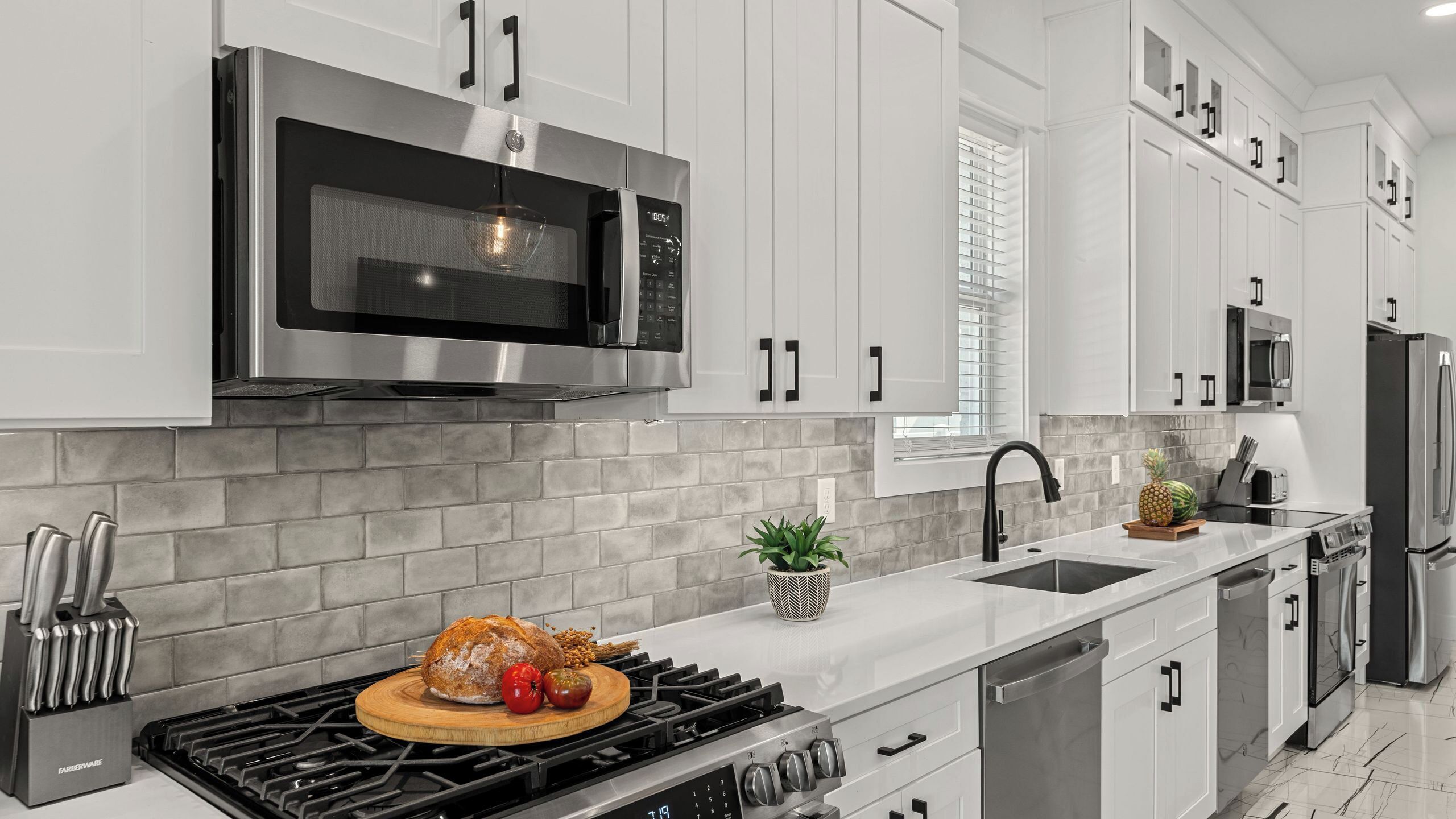 A modern kitchen with white cabinets, a stainless steel microwave, a gas stove, and a sink.