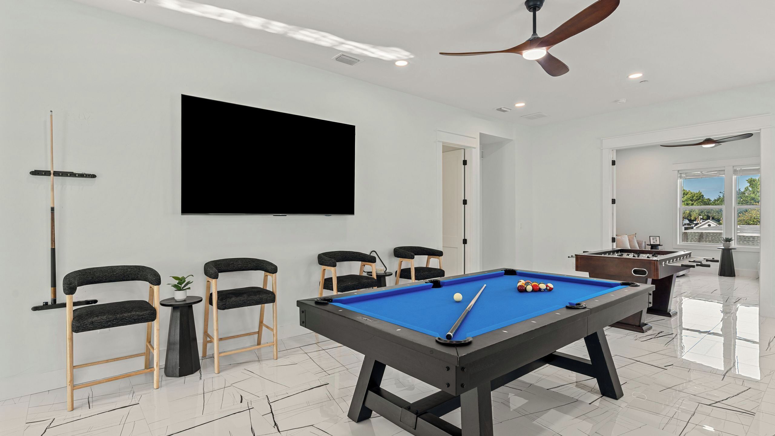 A modern indoor pool table with a blue felt surface, surrounded by four chairs with dark cushions and wooden frames.