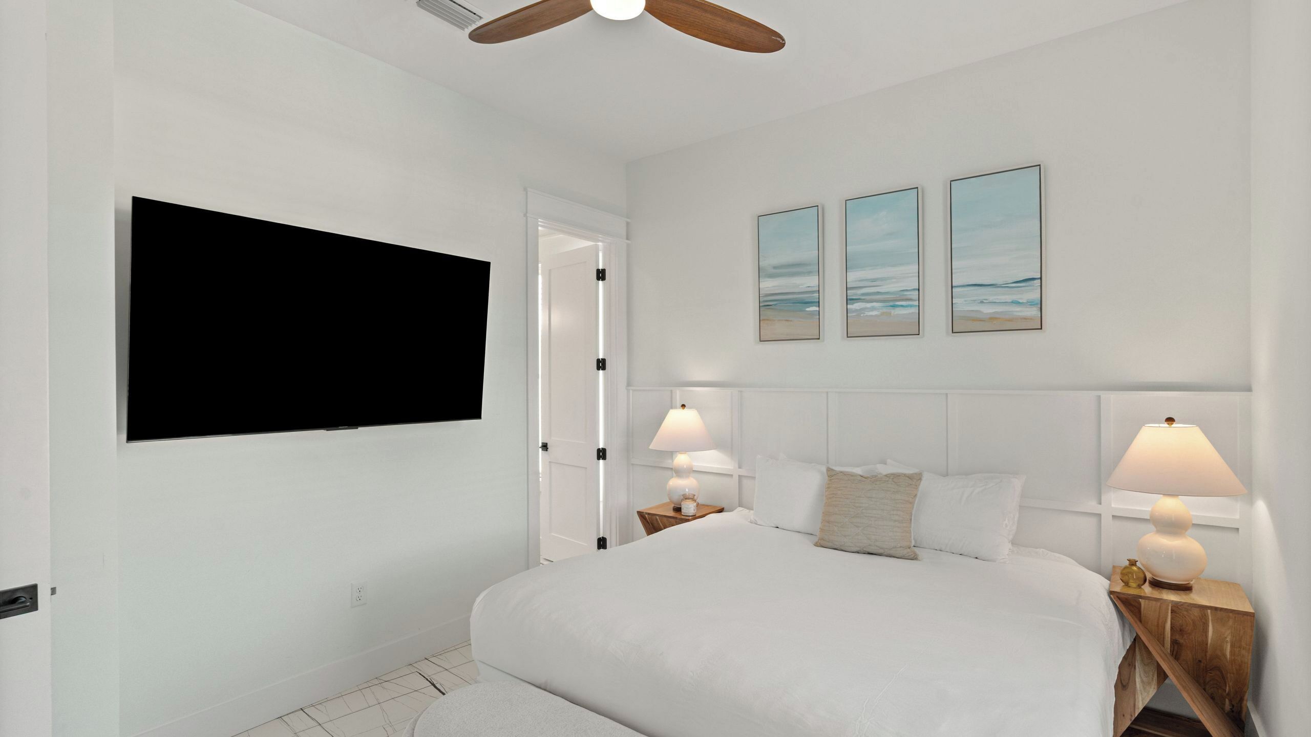 A bedroom with a bed, bedside lamps, a TV, and two wall-mounted paintings.