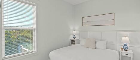 A bedroom with a large bed, two bedside tables with lamps, a ceiling fan, and a window with blinds.