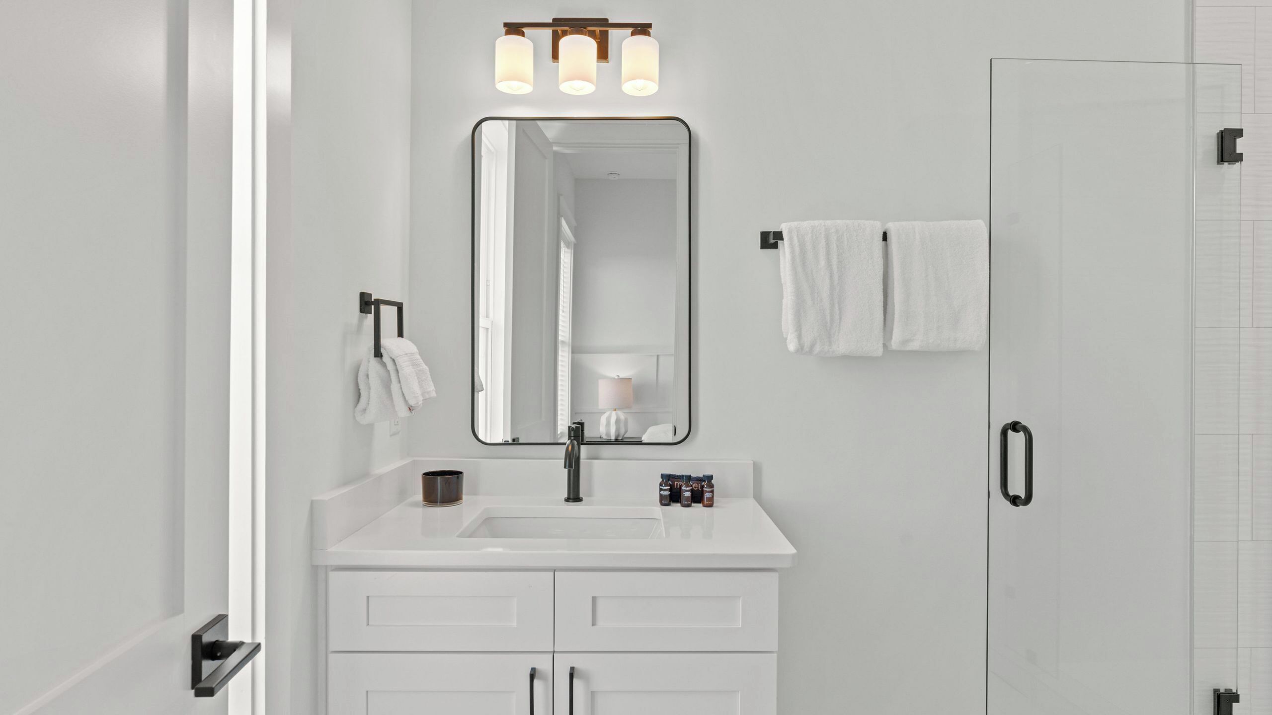 A modern bathroom with a white vanity, a large mirror, and a shower door.