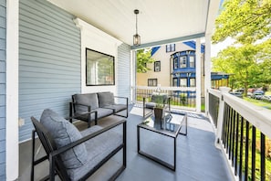 A covered porch with a sofa and coffee table, a hanging light fixture, and a view of a blue building with a bay window.