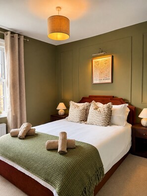 Een hotelkamer met een groot bed, twee nachtkastjes met lampen, een hanglamp en een foto in een lijst aan de muur.