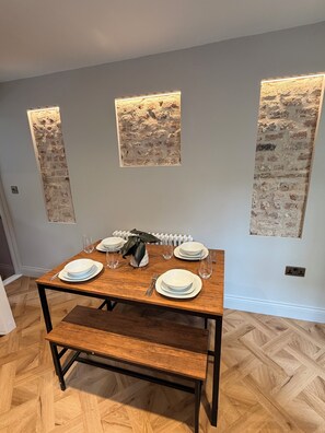 Een eetgedeelte met een houten tafel voor vier personen, begrensd door gestructureerde wandpanelen.