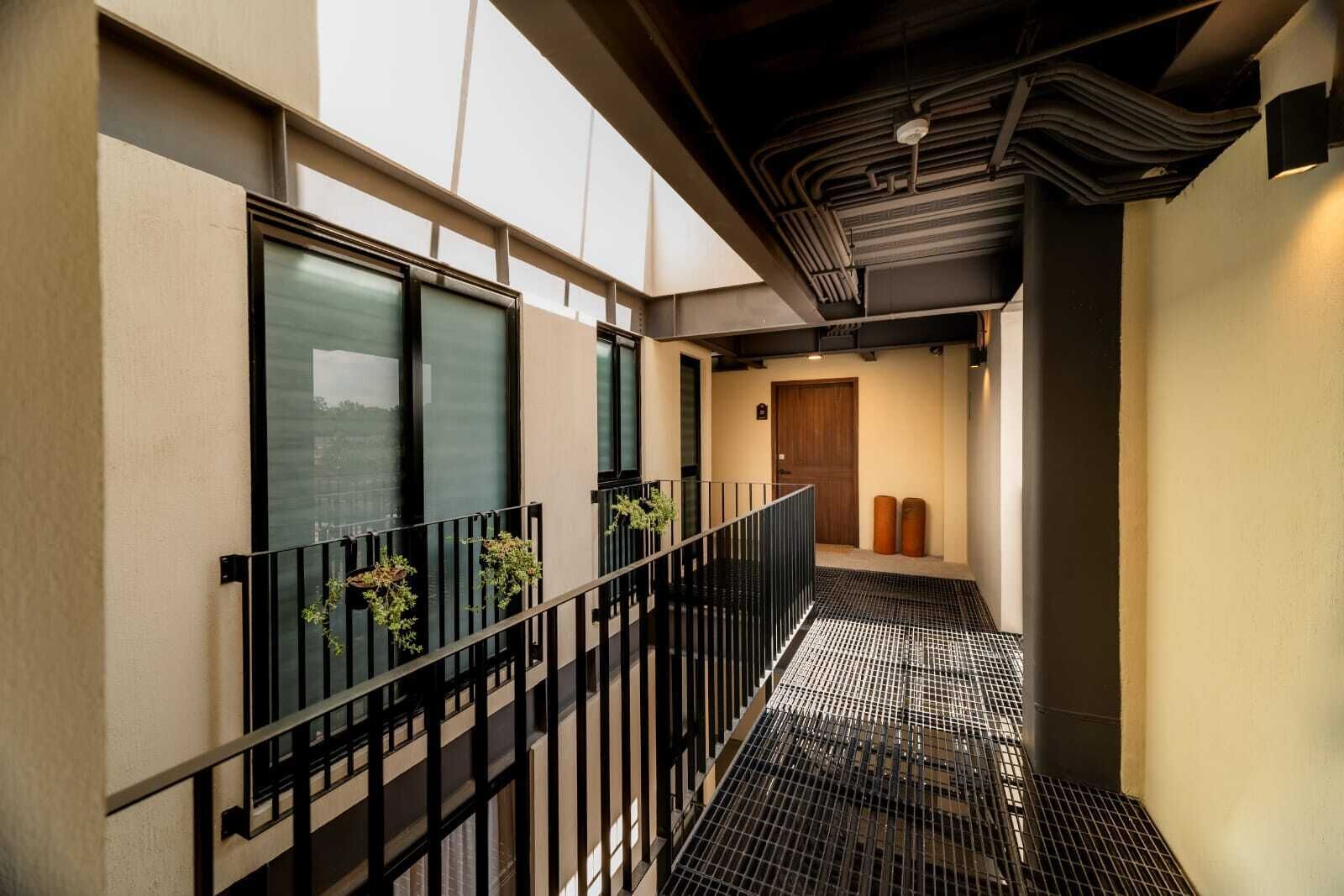 A corridor with a metal railing, a wooden door, and a small plant on the railing.