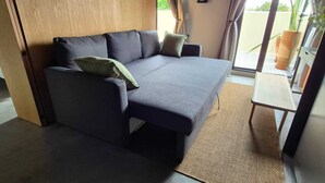 Une chambre moderne avec un canapé, une petite table et une vue sur l’extérieur, visible à travers une porte vitrée.