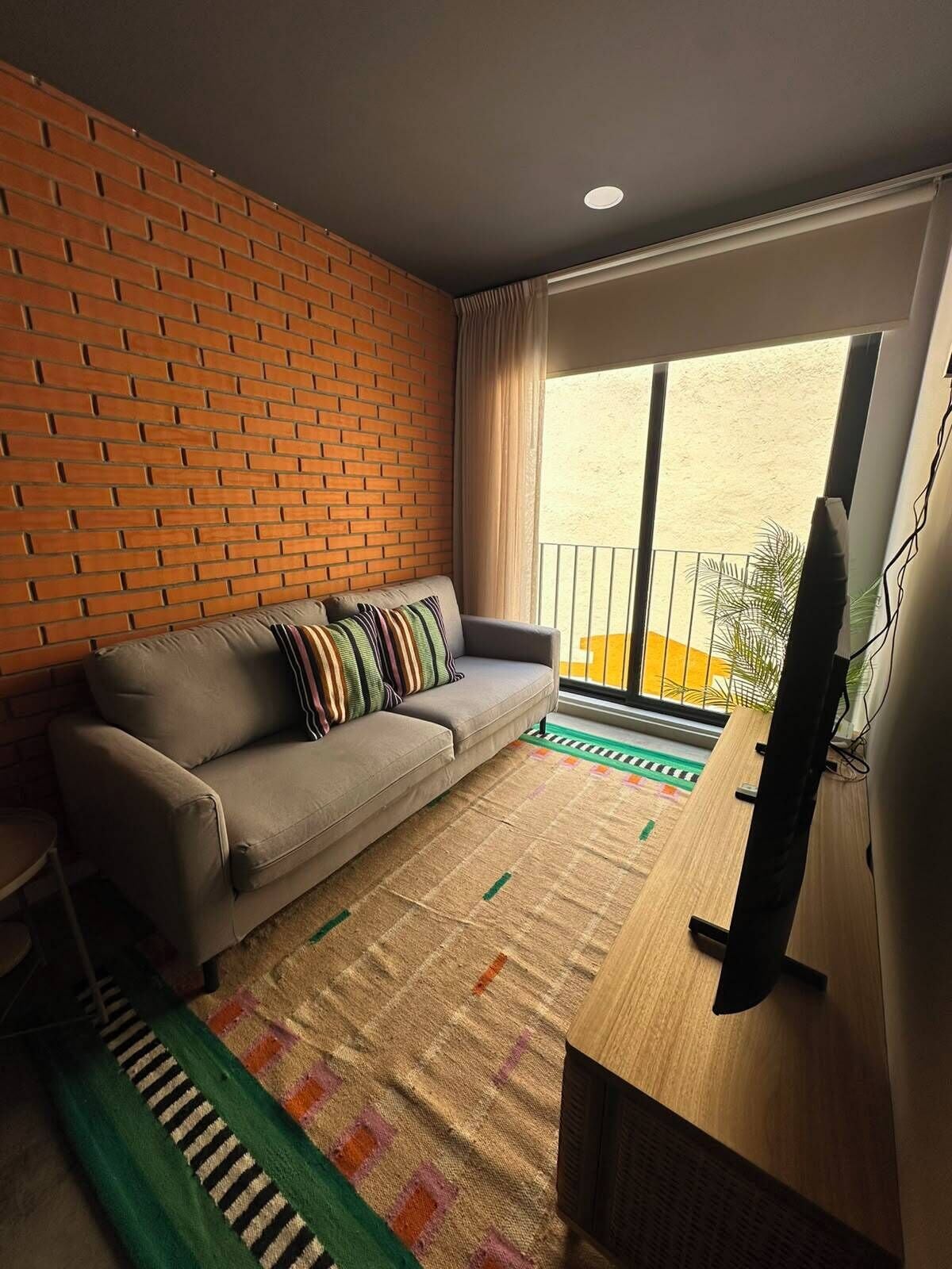 A living room with a sofa, a television, a patterned rug, and a brick wall.