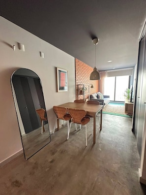 Un comedor moderno con una pared de ladrillo decorativa, una mesa de madera, sillas de mimbre y una lámpara colgante.