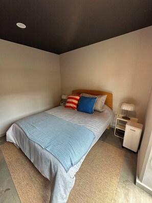 A single bed with a grey and blue bedspread, a wooden headboard, and two bedside tables with lamps. - Tradere (Zapopan)