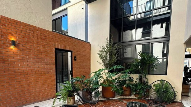 Une cour avec un sol en briques, un banc, des plantes en pot et un bâtiment doté de grandes fenêtres et de balcons.
