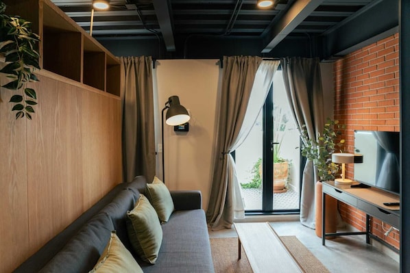 Una sala de estar moderna con un sofá, un escritorio, un televisor y vistas al exterior.