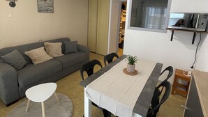 A living room with a gray sofa, a small round table, a dining table with chairs, a ceiling light, a wall-mounted TV, and a microwave. - Studio with private bathroom for 4 people at the base of the gondola (Cauterets)