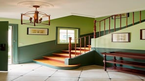 Un escalier avec des marches en bois et une rampe en bois, menant à un palier agrémenté d’un lustre.