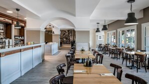 A spacious restaurant with a long counter, multiple tables, and hanging pendant lights.
