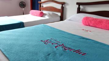 Two single beds with wooden headboards, a teal blanket with embroidered text, and a pink pillow on one bed.