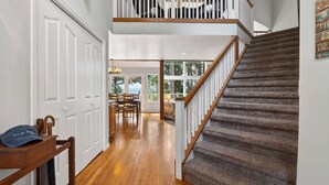 A staircase with wooden steps and a railing, leading to a room with a view of trees. - Cedar & Sound by Avantstay Indoor Hot Tub + Game Room + Media Room Sound + Olympic Mtn Views (Freeland)