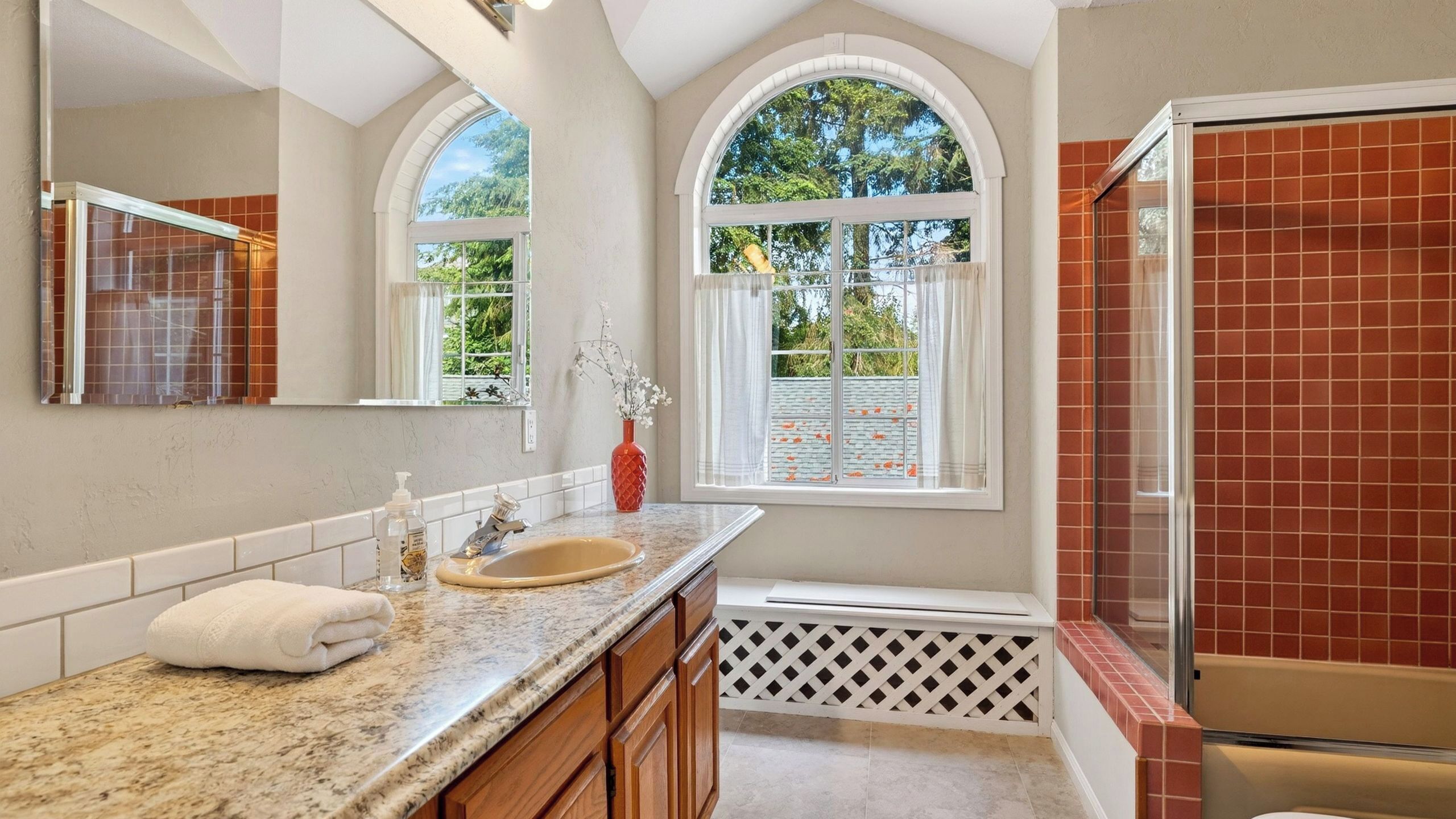 Une salle de bain avec un grand miroir, un lavabo, une fenêtre et un espace douche.