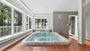 Ein Whirlpool in einer überdachten Außenbereich mit großen Fenstern und Blick auf Bäume.