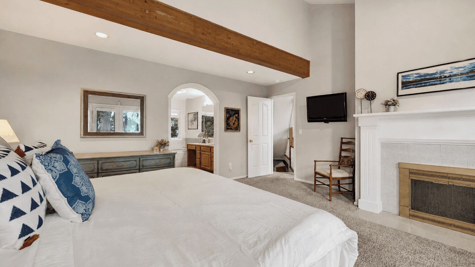 Une chambre avec un grand lit, une cheminée, une télévision et un couloir menant à une salle de bain.