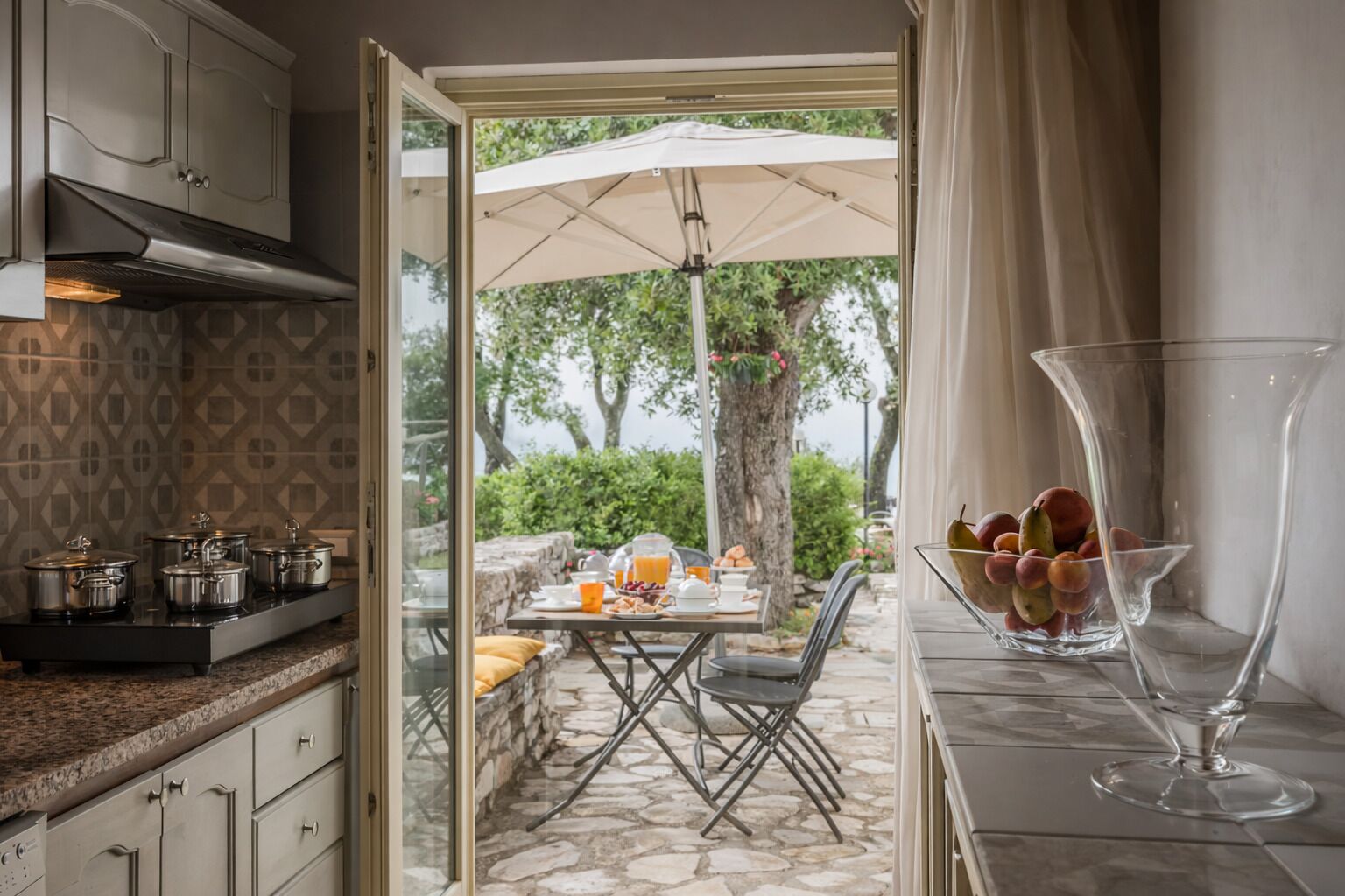 Uma cozinha com bancada de pedra, uma área de jantar com mesa e cadeiras, e um guarda-sol grande.