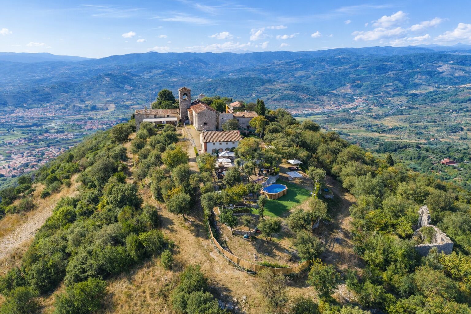 A hilltop property with a stone building, a swimming pool, and a fenced garden.