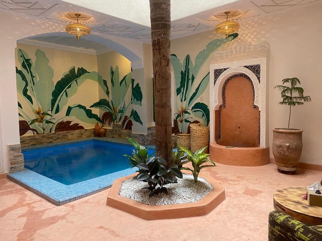 Una zona de piscina amb sòl de rajola, una palmera i una gran planta en test.