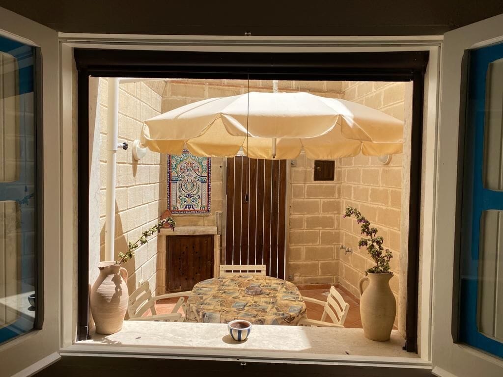 A room with a table under a large umbrella, a vase, and a potted plant.