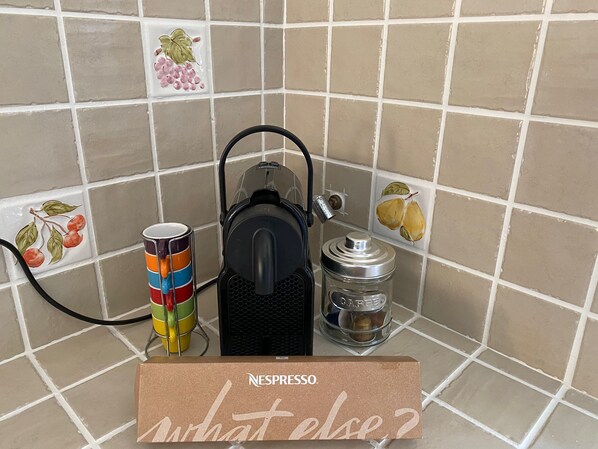 A Nespresso machine, a colorful mug, and a coffee grinder on a tiled kitchen counter.