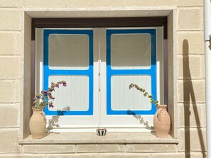 A window with two white panels and blue borders, flanked by two ceramic pots with flowers. - A typical fisherman's cottage. (Favignana)