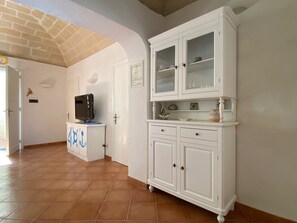 A room with a white cabinet, a television on a stand, and a tiled floor. - A typical fisherman's cottage. (Favignana)