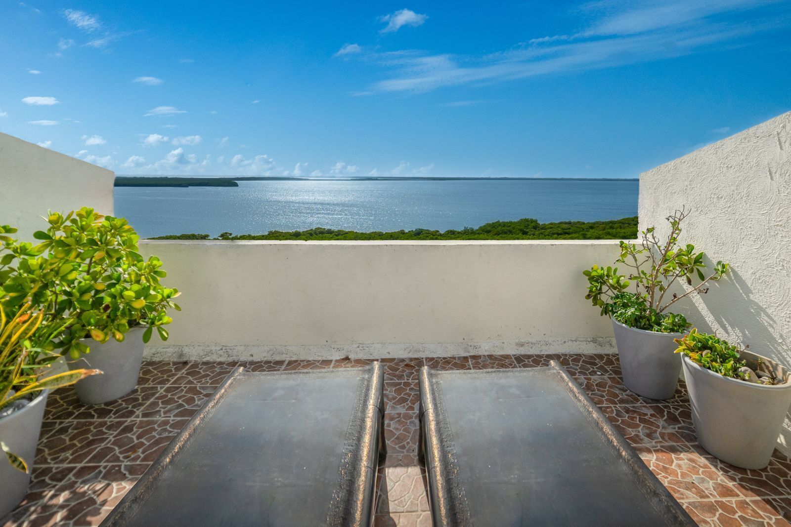 Une terrasse agrémentée de plantes en pot, une vue sur la mer et un sol carrelé.