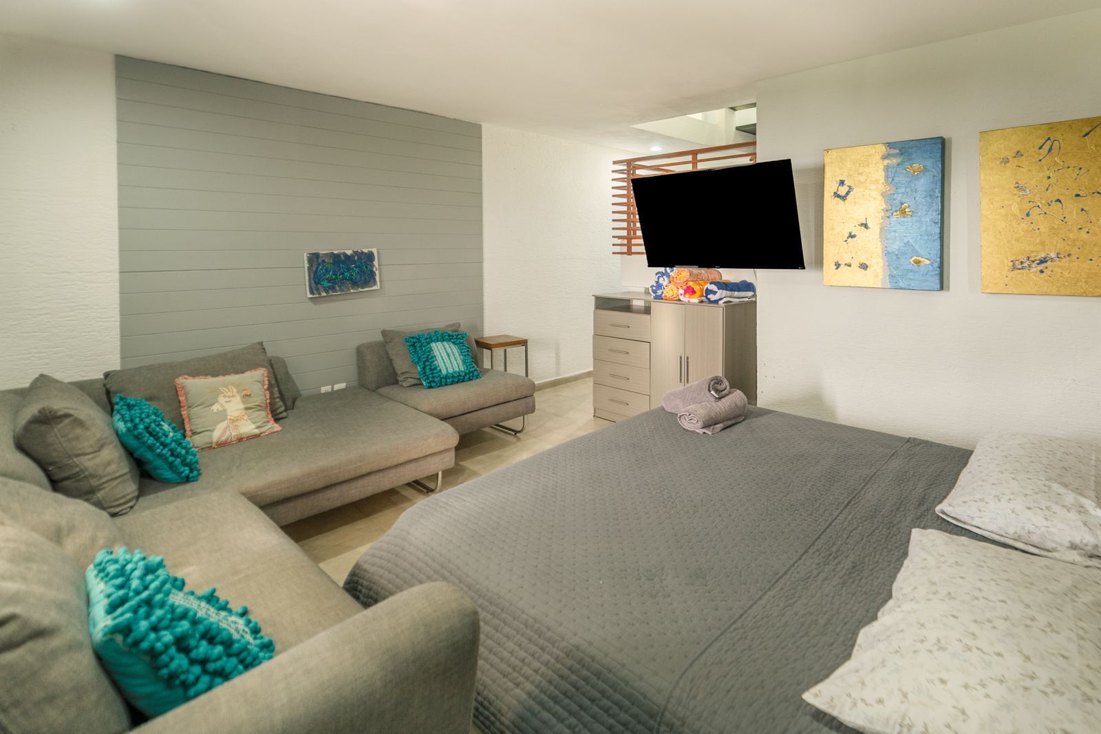A modern bedroom with a sofa, a bed, a TV, and a dresser.