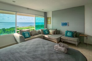 Een moderne slaapkamer met een groot bed, een bank en een dagbed, geplaatst rondom een groot raam met uitzicht op de oceaan.