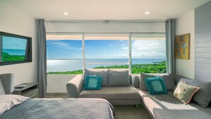 A bedroom with a bed, a sofa, and a large window with a view of the sea and greenery. - Hotel Zone - 3BR - Beach Access 3406 (Cancún)