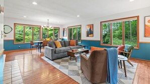 A spacious living room with a large sofa, a coffee table, and a dining area with chairs. - Secluded Mid-Century Haven | Hot Tub | Fire Pit (Fennville)