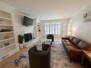 A living room with a fireplace, a television, a brown leather sofa, a coffee table, and a bookshelf.