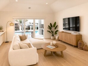 Ein modernes Wohnzimmer mit Sofa, Couchtisch, Fernseher und Blick auf Pool und Außenbereich.