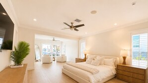 Un dormitorio con cama, mesitas de noche, ventilador de techo y un gran ventanal.