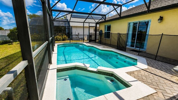 Ein Schwimmbad mit Glasveranda, umgeben von einer gepflasterten Terrasse und einem Haus.