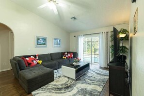 A living room with a sectional sofa, a coffee table, and a television. - House Near Disney: Bambu Magic House (Kissimmee)